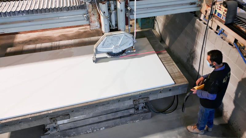 Worker operating a stone-cutting machine to fabricate a large quartz countertop slab during manufacturing